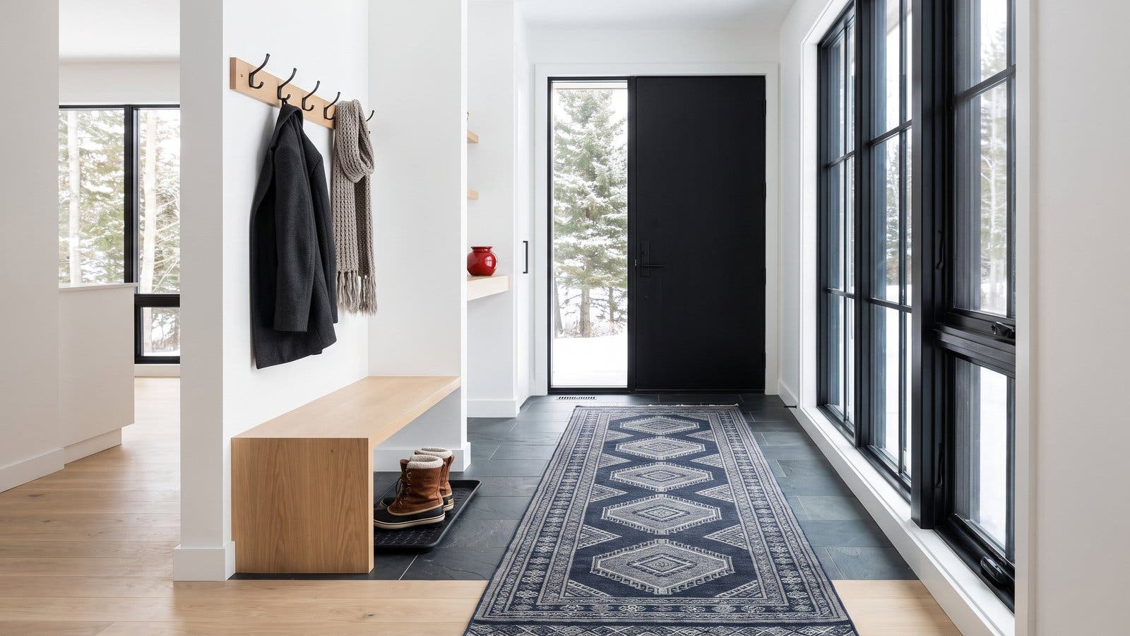 A bright mudroom entry with a long navy runner on slate tile, a white oak bench and winter boots on a tray