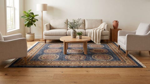 Navy rug with round tan and red floral medallions and a beige border, under a round oak coffee table in a bright living room
