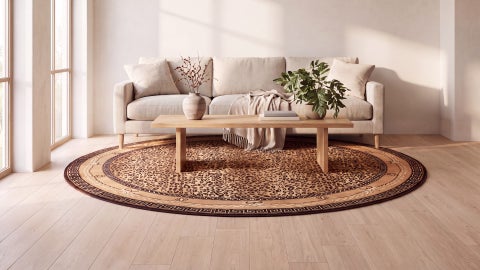 Round tan and brown leopard print rug with a Greek key border on a wood floor under a low table, in front of a cream sofa