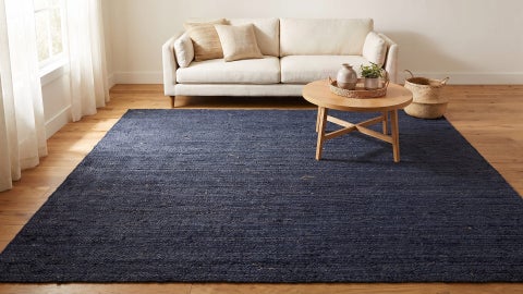 Solid navy braided rug on a wood floor in a living room with a cream sofa, round wooden coffee table and woven basket