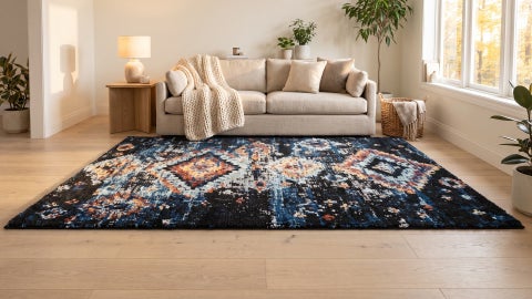 Black and navy rug with faded orange and pale blue diamond patterns on wood floor in front of a cream sofa and knit throw