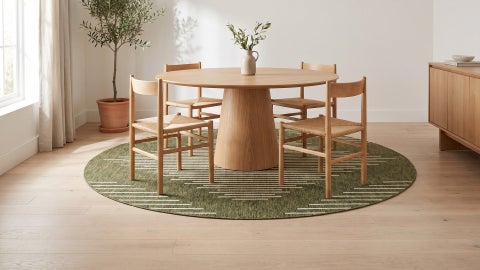 Round olive green rug with cream line pattern under a wooden round dining table and four chairs on a light wood floor